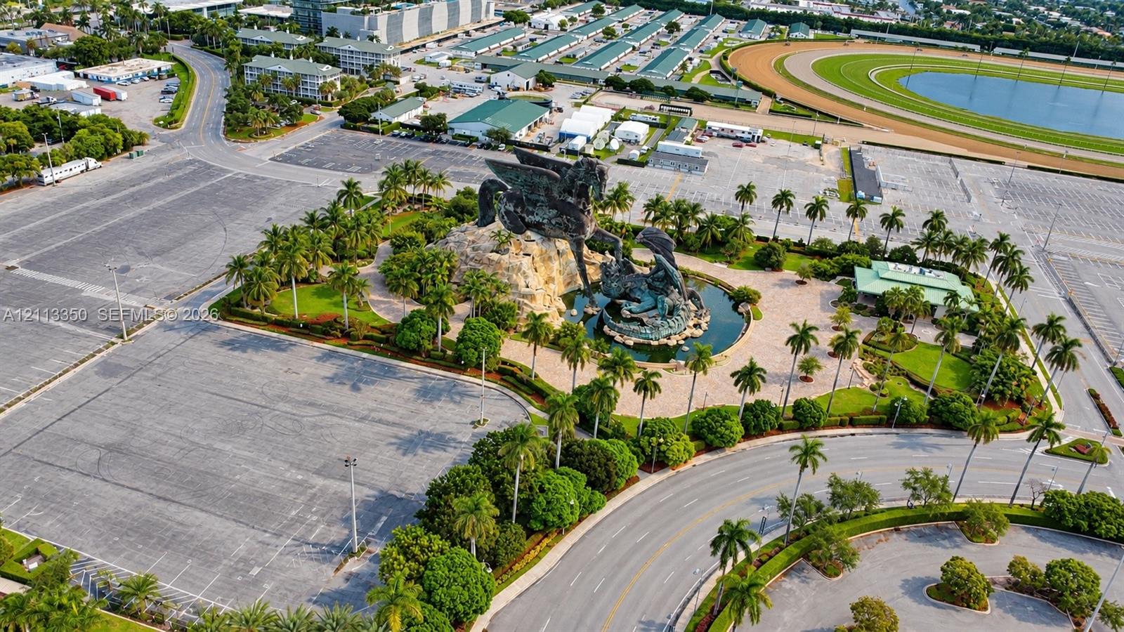 Aerial perspective featuring a large-scale sculptural monument, central water feature, mature palm landscaping, and expansive paved grounds