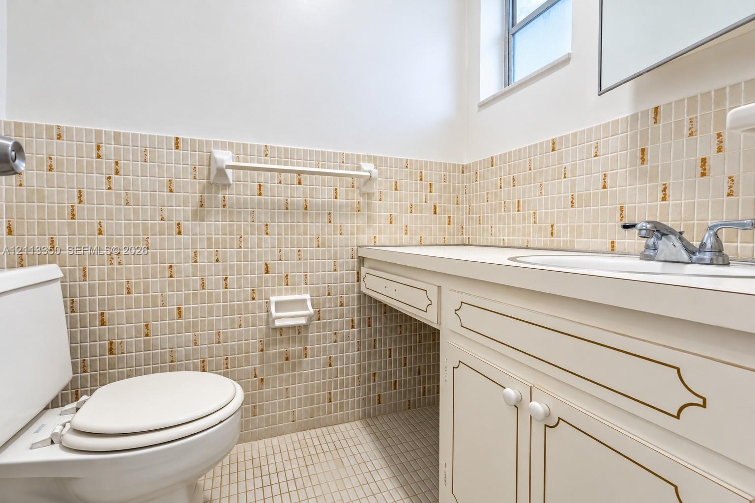 Bathroom featuring a vanity with white cabinetry and decorative trim, a solid surface countertop with an integrated basin, and mosaic tile wall accents