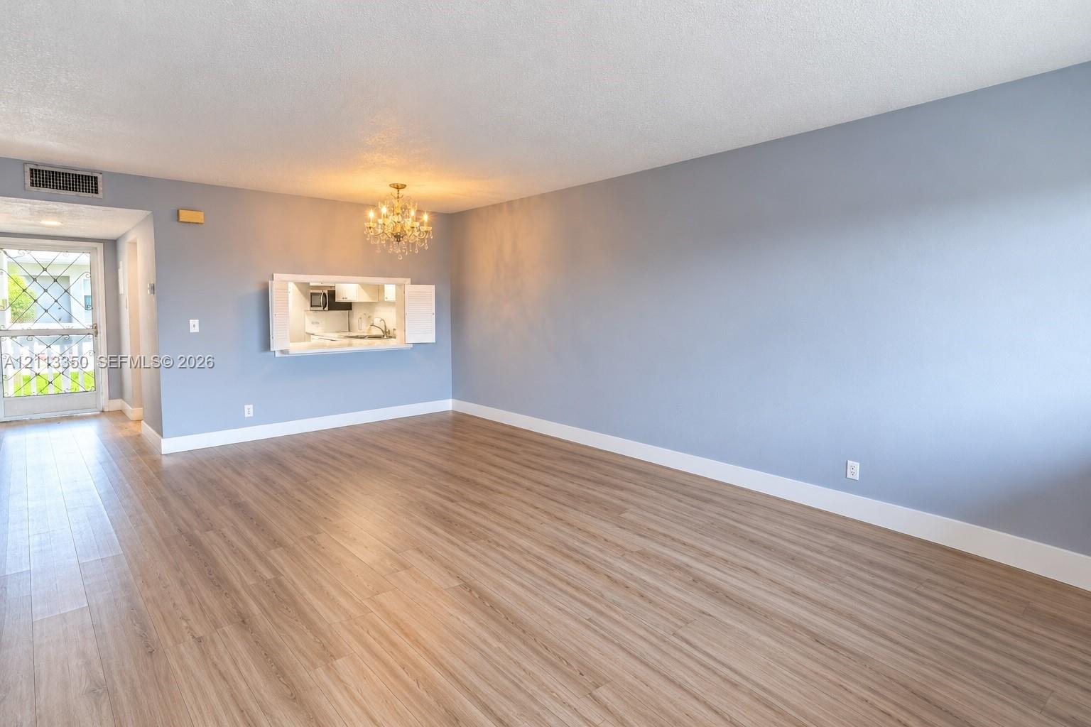 Open-concept living space featuring wood-finish flooring, a crystal chandelier, and a pass-through window with built-in cabinetry