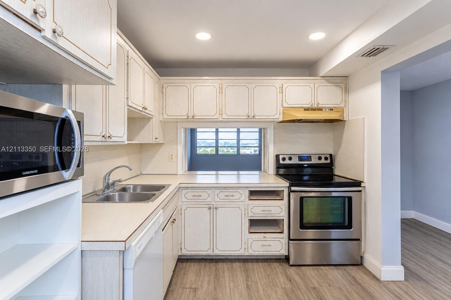 Kitchen featuring light-finish cabinetry, stainless steel microwave, stainless steel range, double-basin sink with arched faucet, and recessed ceiling lighting