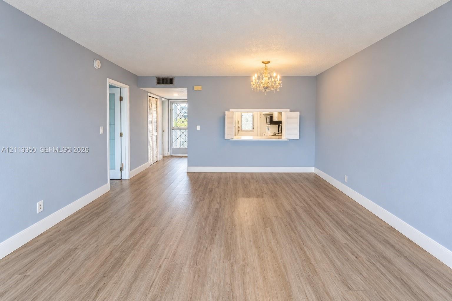Open-concept room featuring wood-finish flooring, a pass-through window with cabinet doors, a crystal-style chandelier, and glass-paneled entry doors
