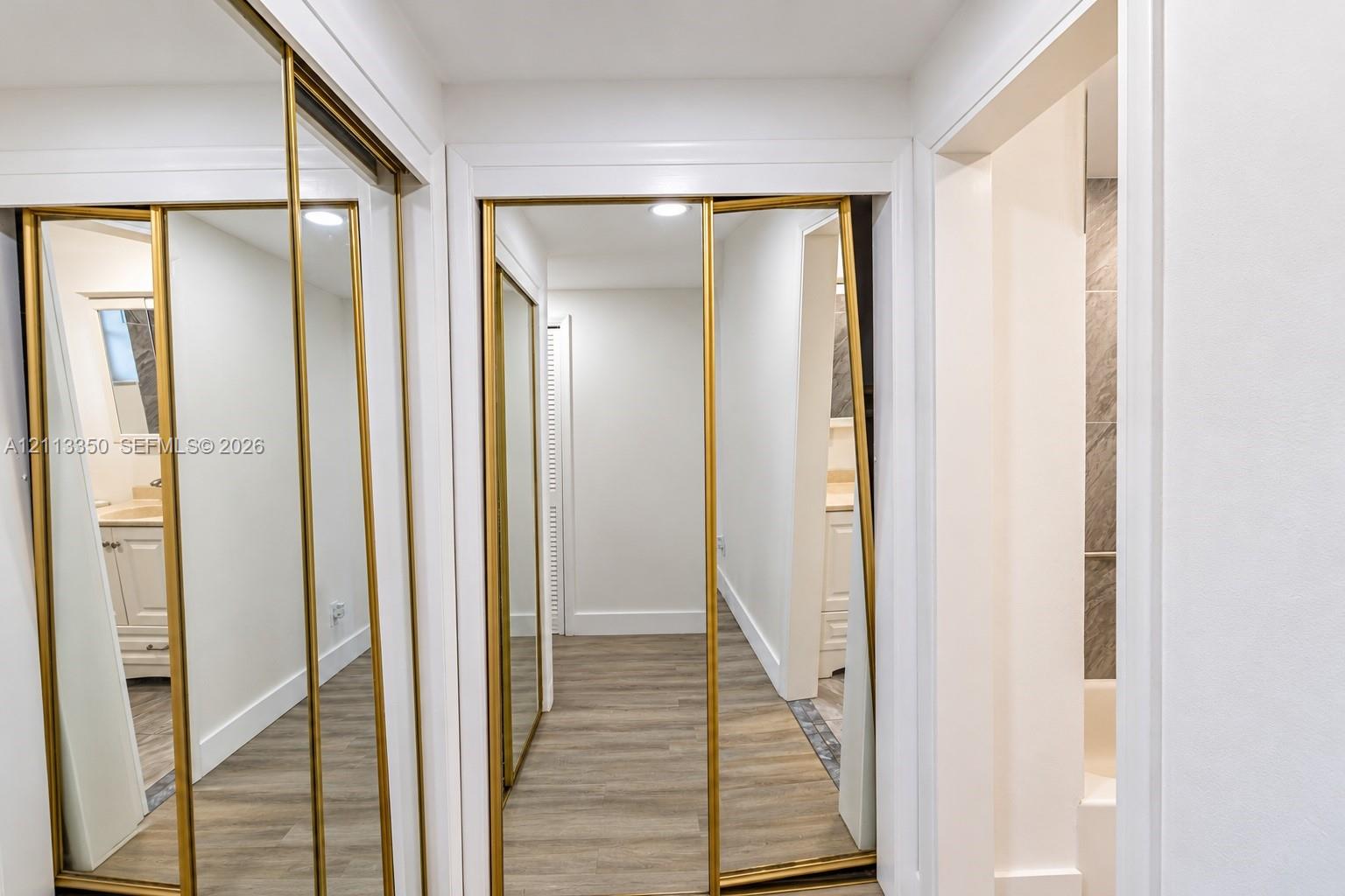 Wall-to-wall mirrored closet doors with gold-toned metal trim, wood-finish flooring, and recessed ceiling lighting