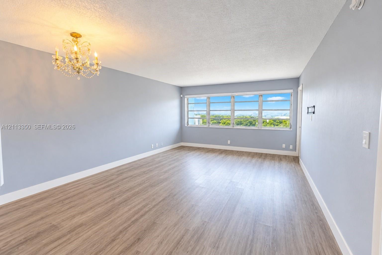 Expansive room featuring wood-finish flooring, multi-pane windows, and a decorative chandelier