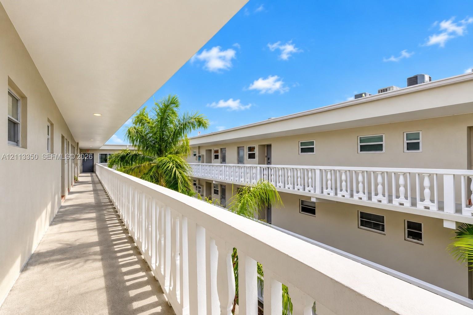 Exterior walkway featuring a concrete floor, white balustrade railings, and mature palm trees