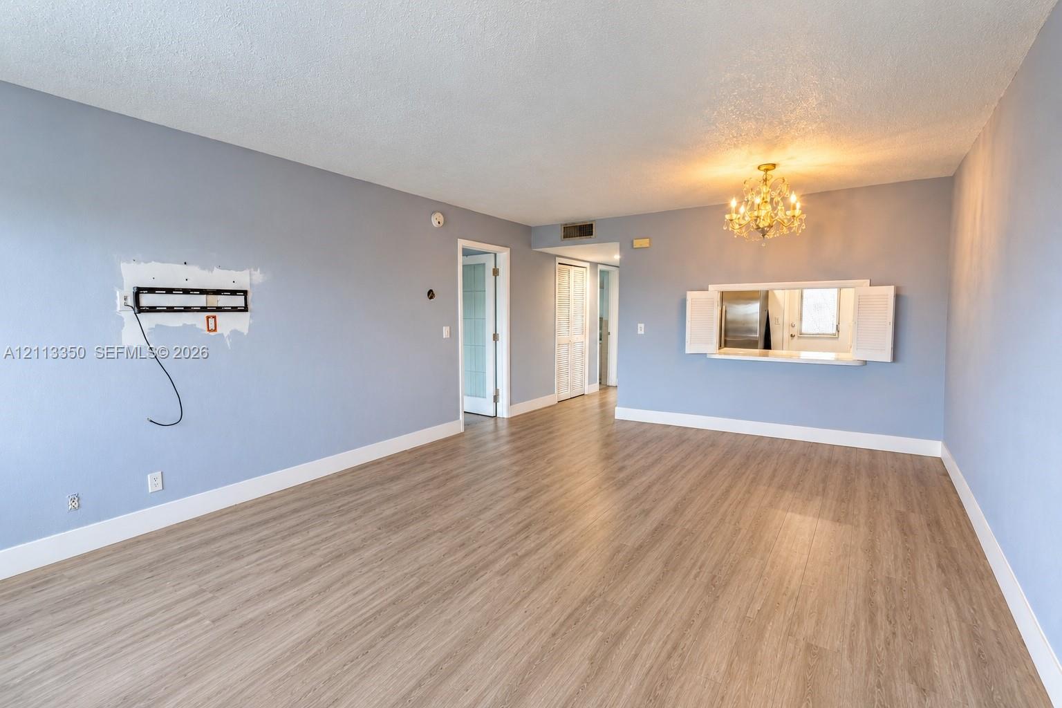 Wood-finish flooring, pass-through opening to kitchen, ornate chandelier, and paneled doors