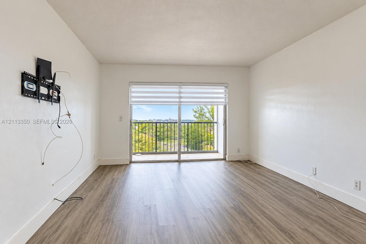 Wood-finish flooring, white walls, sliding glass door with dual-tone roller shade, and metal-railing balcony