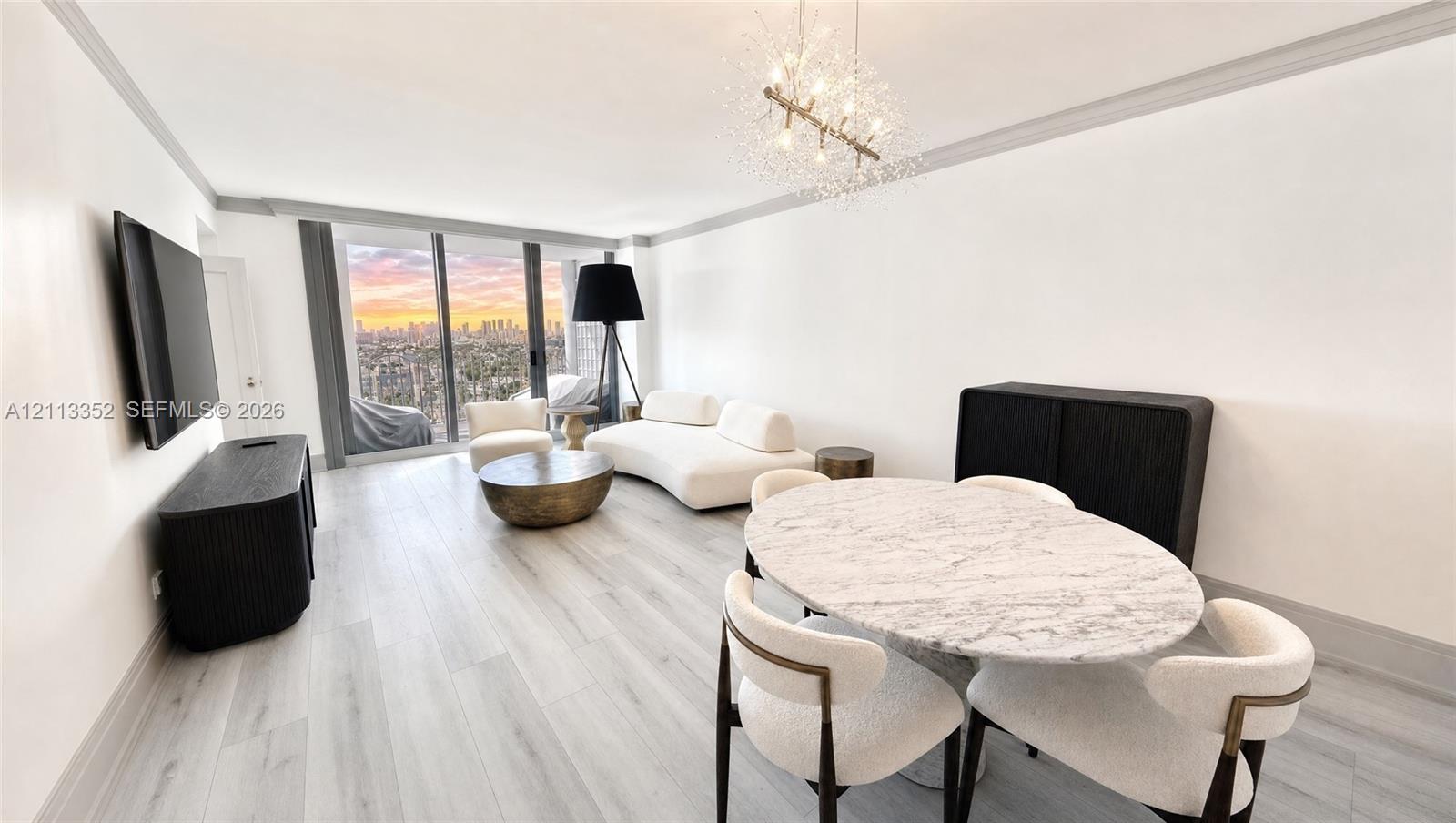 Open-concept living space featuring wood-finish flooring, floor-to-ceiling windows, a metallic starburst chandelier, crown molding, and an expansive cityscape backdrop