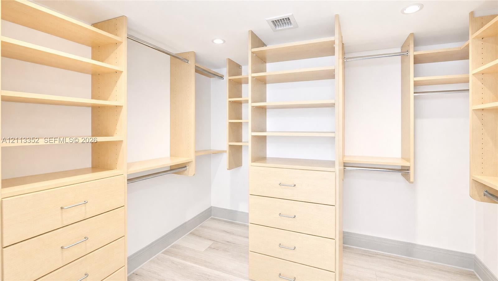 Custom walk-in closet featuring extensive light-finish wood cabinetry, integrated drawer banks, multiple tiered open shelving units, and metal hanging rods