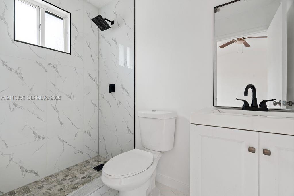 Bathroom featuring a walk-in shower with stone-patterned tile walls, pebble-style flooring, a matte black rainfall showerhead, a white shaker-style vanity, and a framed mirror