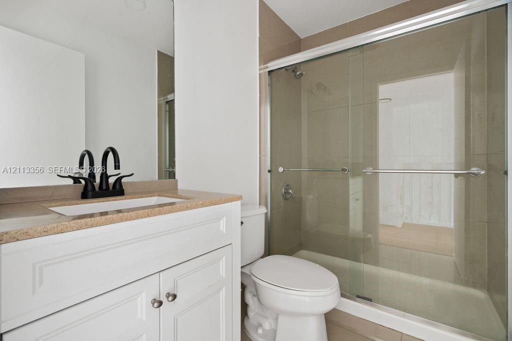 White vanity cabinet with a stone-finish countertop, integrated rectangular sink, matte black faucet, and a shower enclosure featuring sliding glass doors and neutral tile surround