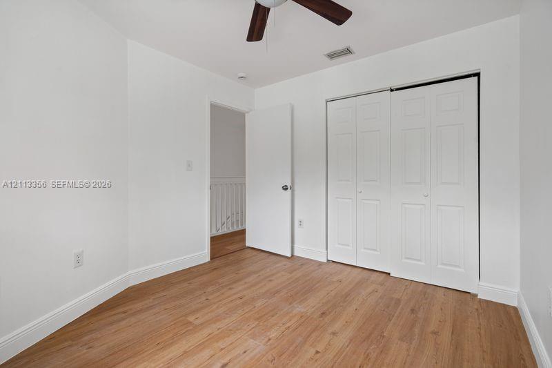 Room featuring wood-finish flooring, a ceiling fan with integrated lighting, and a closet with white paneled bi-fold doors