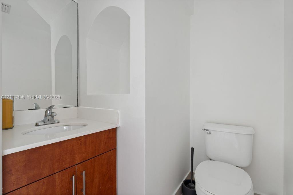 Wood-finish vanity cabinet, solid-surface countertop with integrated sink, polished chrome faucet, rectangular wall-mounted mirror, and an arched architectural recessed niche