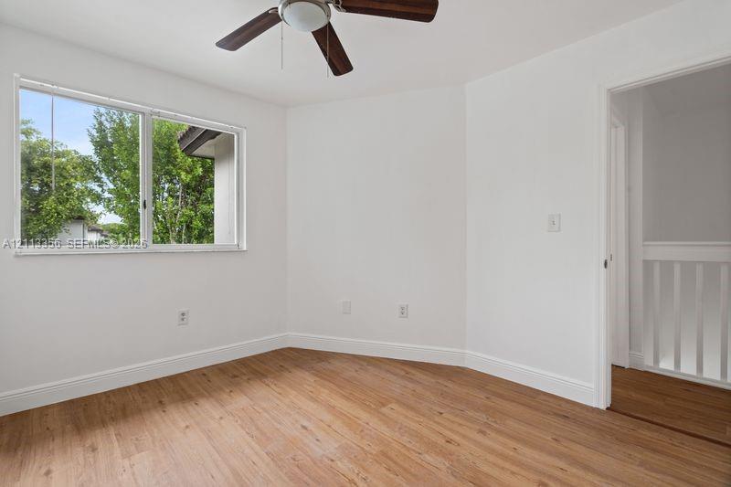 Room featuring wood-finish flooring, a ceiling fan with integrated lighting, and a window with horizontal blinds