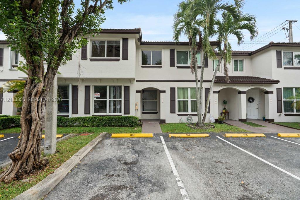 Two-story exterior featuring light-toned stucco, dark-toned shutters, multiple windows with grid detailing, and arched entryways