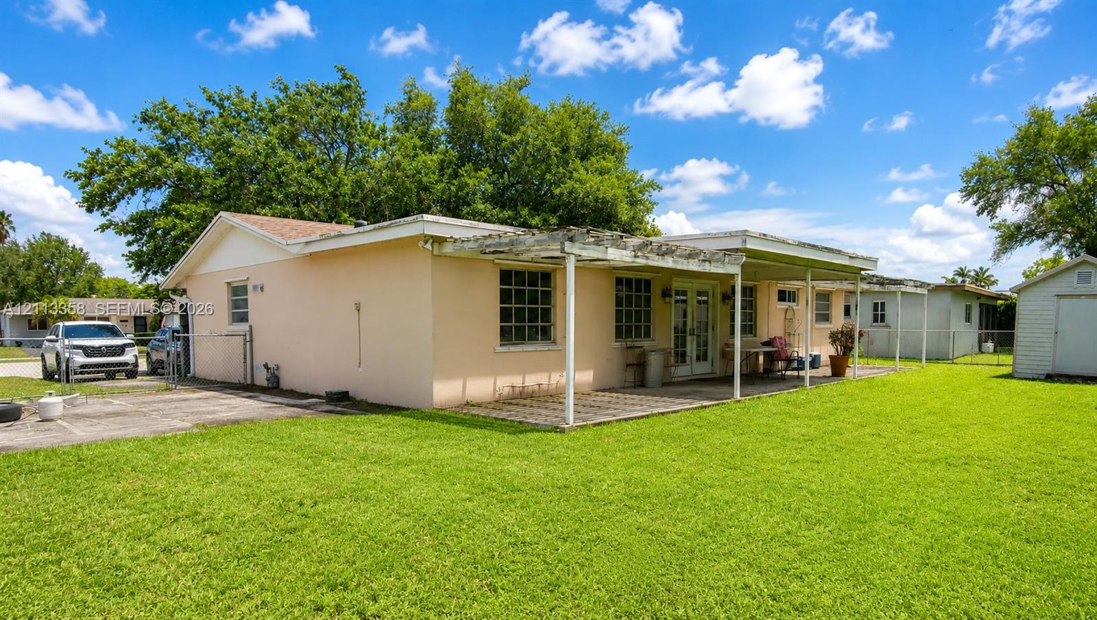 Exterior of the residence featuring a concrete patio with a pergola, exterior French doors, a concrete driveway, and a detached storage structure