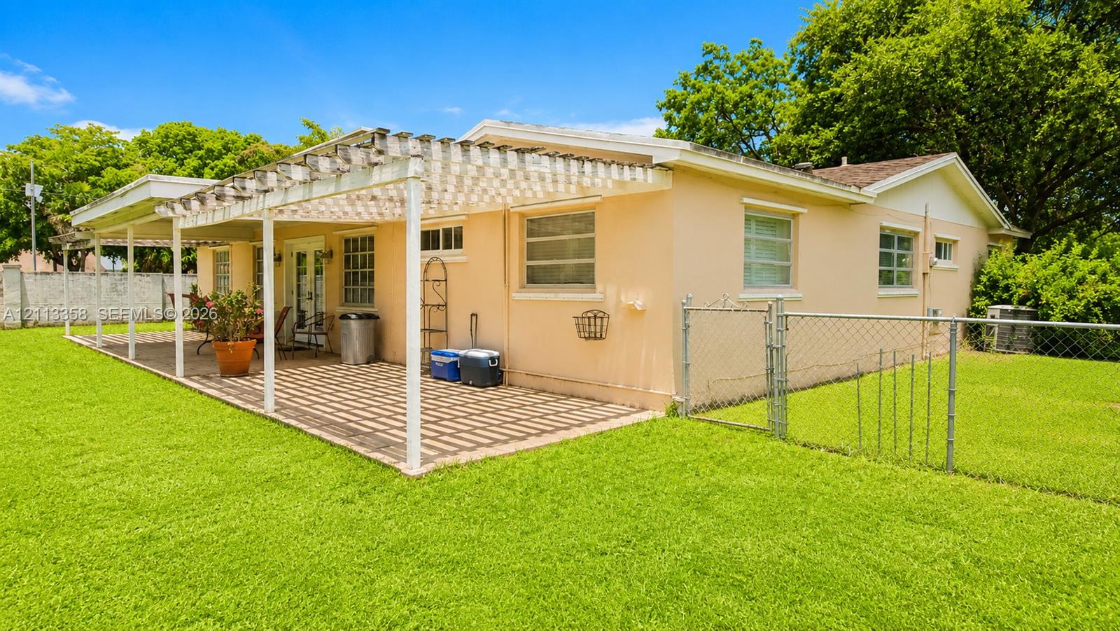 Exterior space featuring a covered patio with a wooden pergola, brick paver flooring, a chain-link fence, and an expansive lawn