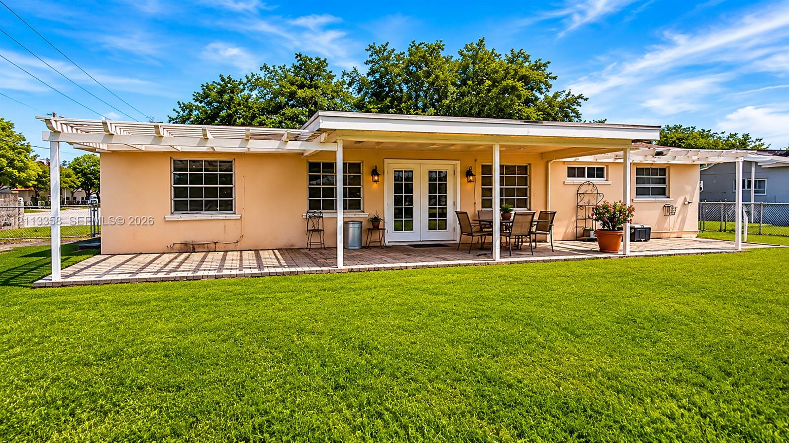 Rear exterior featuring an expansive lawn, a covered patio with a paved surface, and dual pergola structures