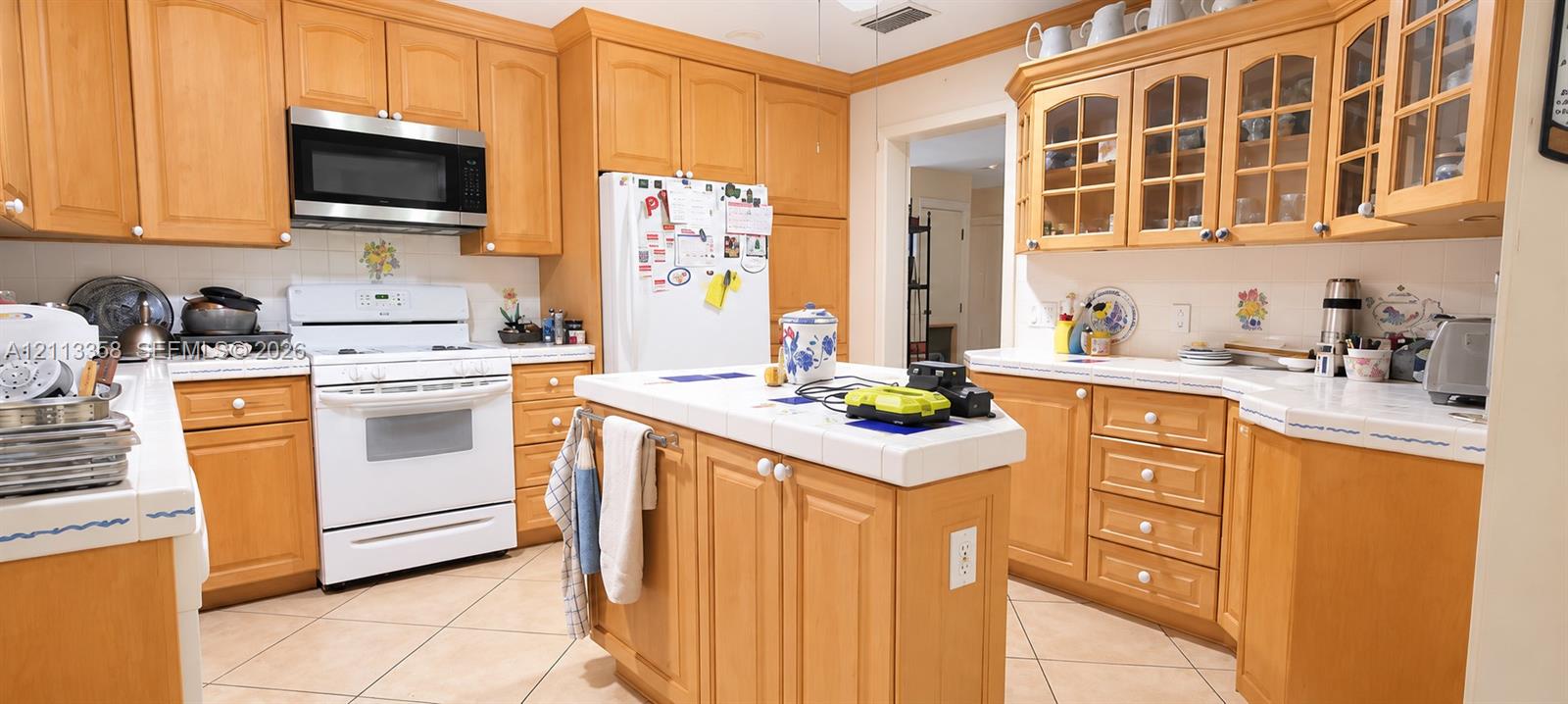 Kitchen featuring natural wood cabinetry, central island with tiled countertop, glass-front upper cabinetry, and tile flooring
