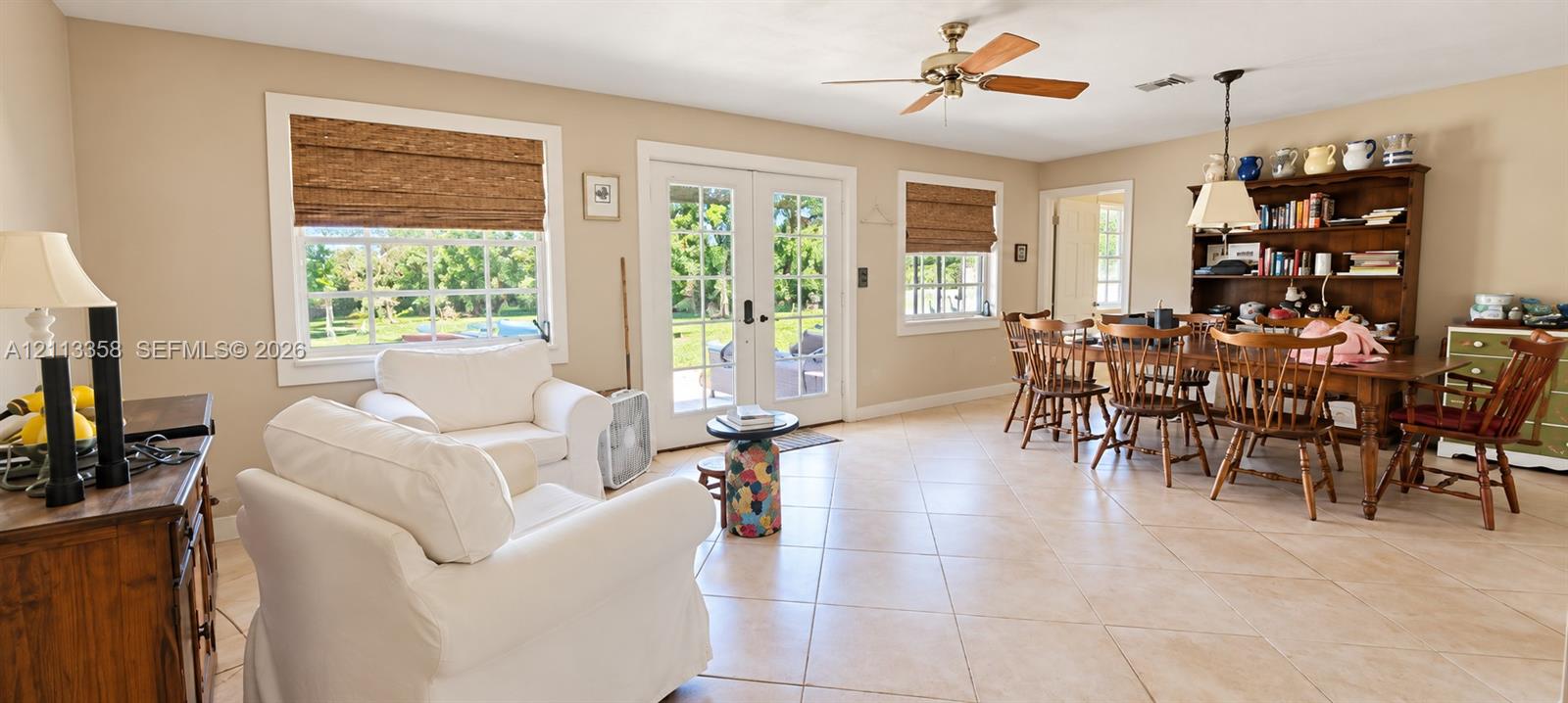 Open-concept area featuring light-toned tile flooring, dual glass-paned French doors, multi-pane windows, and a ceiling-mounted fan