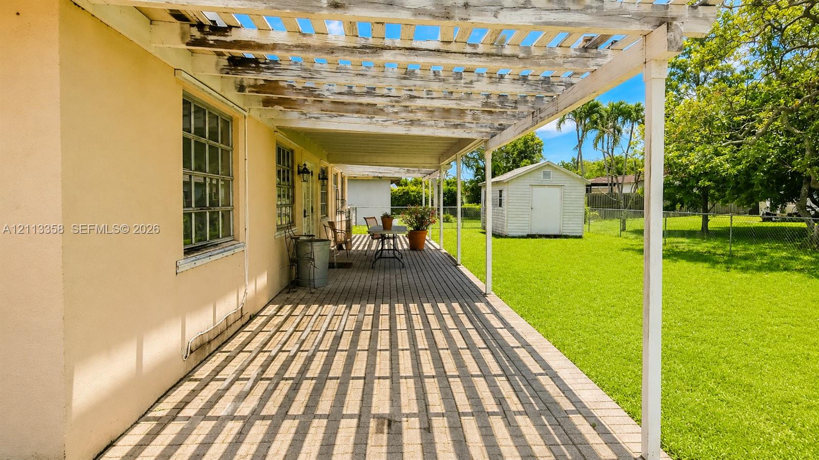Covered patio with a wood-slat pergola, paved flooring, and a fenced backyard featuring a detached storage structure