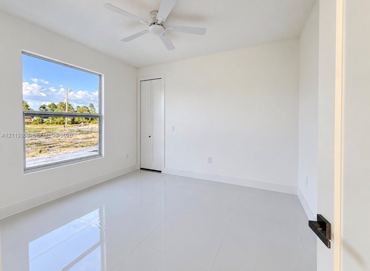 Interior space featuring large-format tile flooring, crisp white walls, a ceiling fan, and a bi-fold closet door