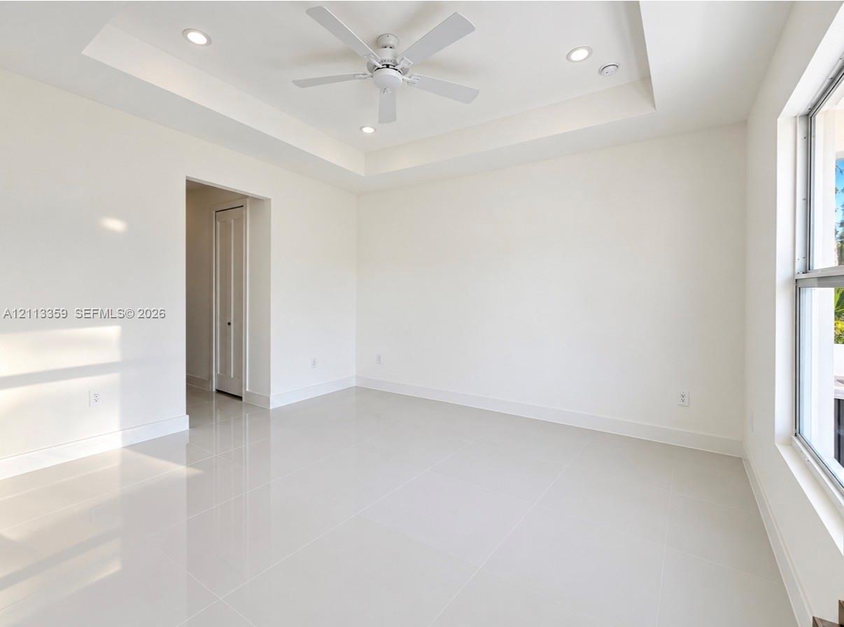 Tray ceiling featuring a central white ceiling fan, recessed lighting, and large-format tile flooring