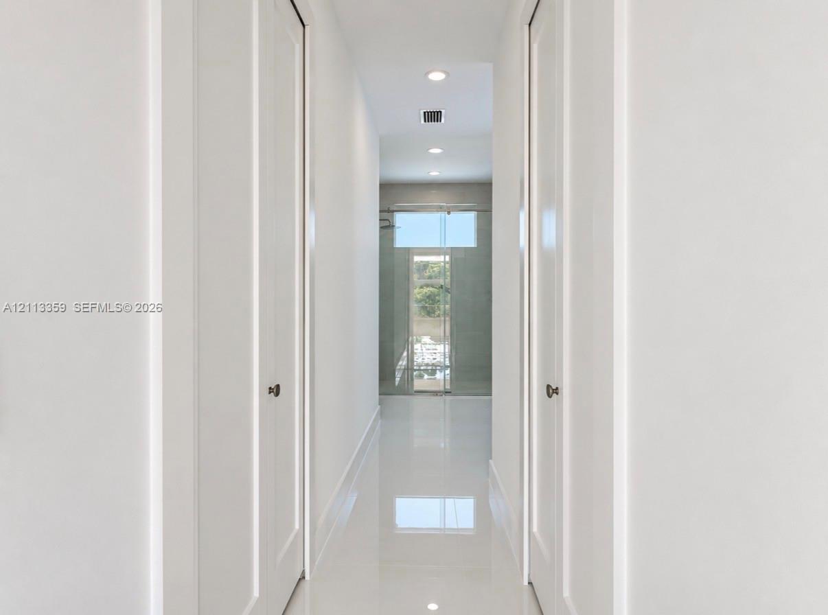 Hallway featuring high-gloss tile flooring, recessed ceiling lighting, and dual floor-to-ceiling closets with paneled doors