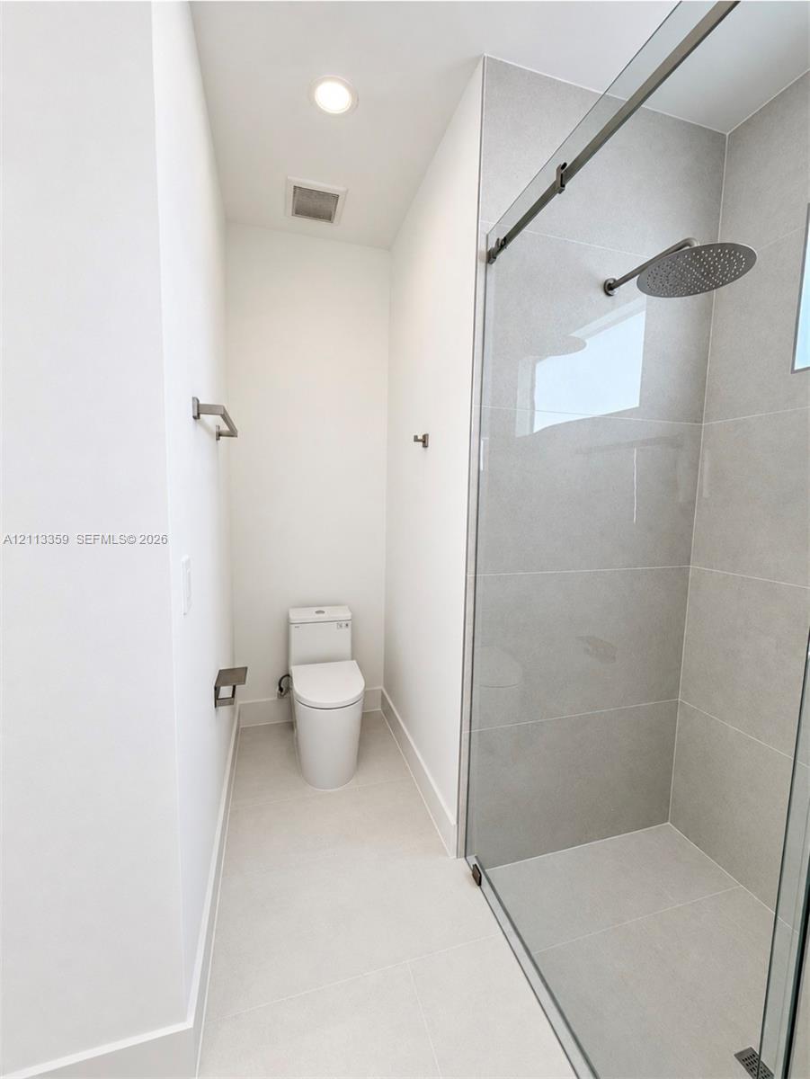 Walk-in shower featuring large-format ceramic wall tile, a glass sliding enclosure, and a ceiling-mounted rainfall showerhead, complemented by a dual-flush elongated toilet
