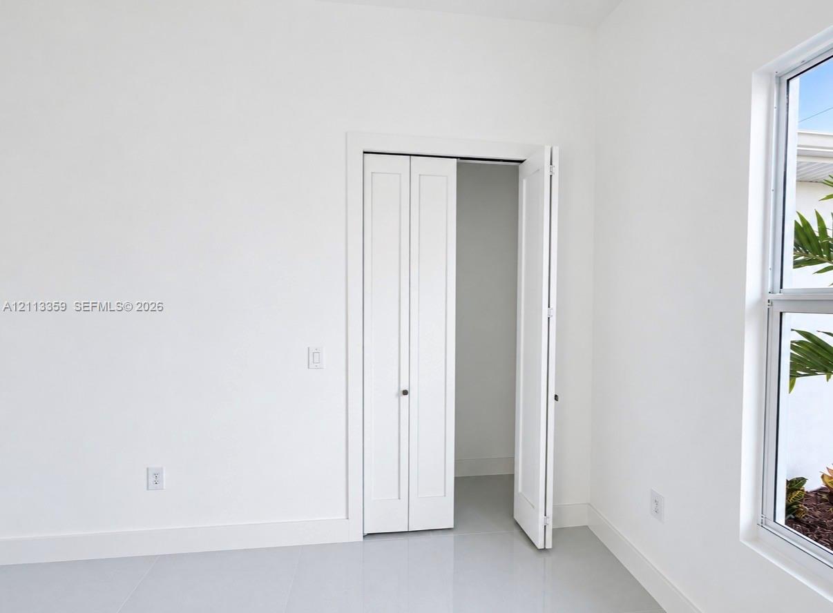 Neutral-toned tile flooring, white-finished walls, and a multi-panel bifold closet door