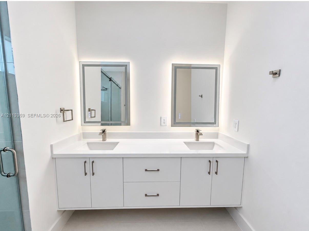 Floating double vanity featuring a white countertop with dual undermount sinks, satin-finish faucets, built-in lower cabinetry, and two rectangular LED-backlit mirrors