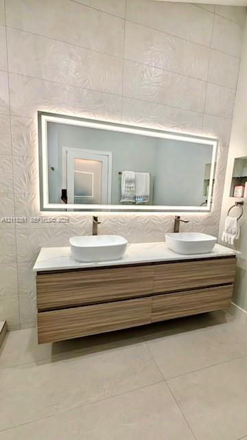 Walk-in shower featuring a frameless glass enclosure, pebble-stone flooring, and textured wall tile, paired with a floating wood-finish vanity and illuminated mirror