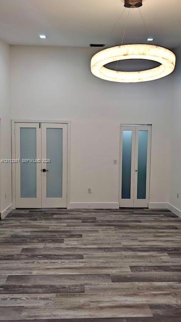 Hallway featuring wood-finish flooring, high ceilings, glass panel railing, and white louvered closet doors