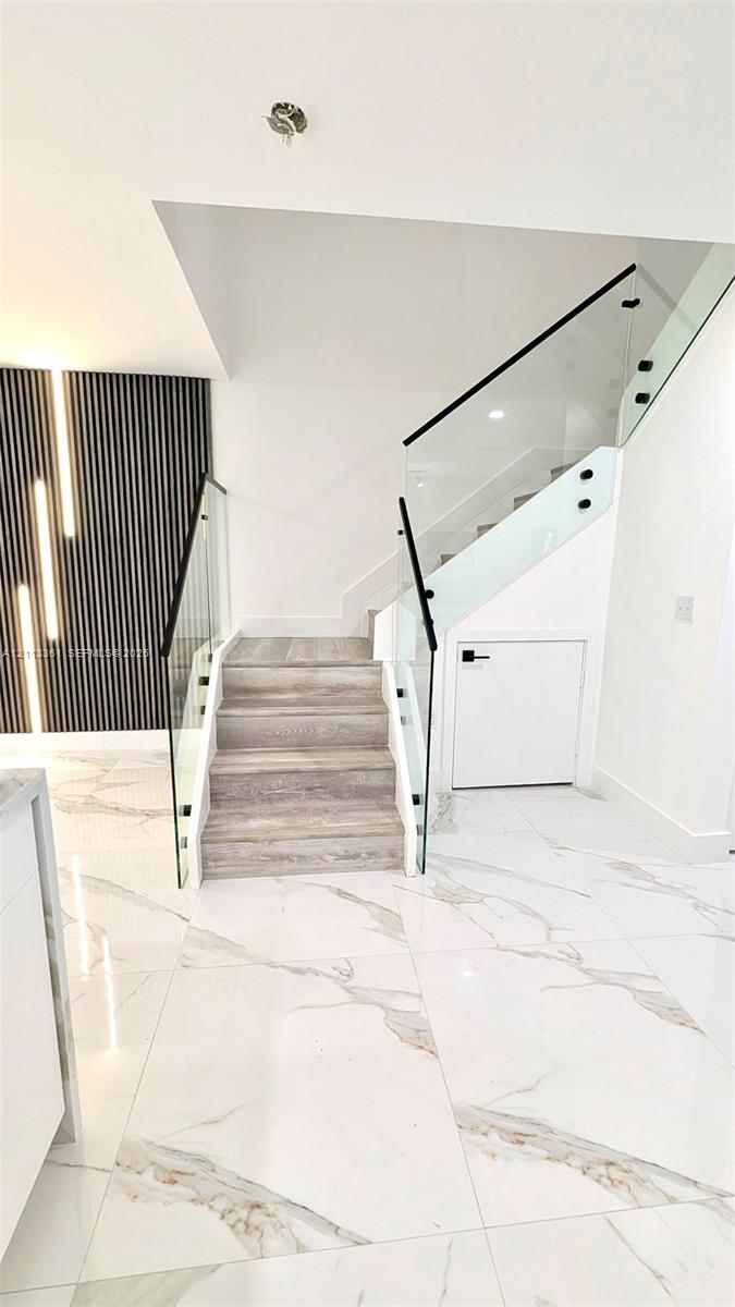 Staircase featuring wood-finish treads, frameless glass railings with black hardware, and vertical slat accent wall paneling over large-format tile flooring