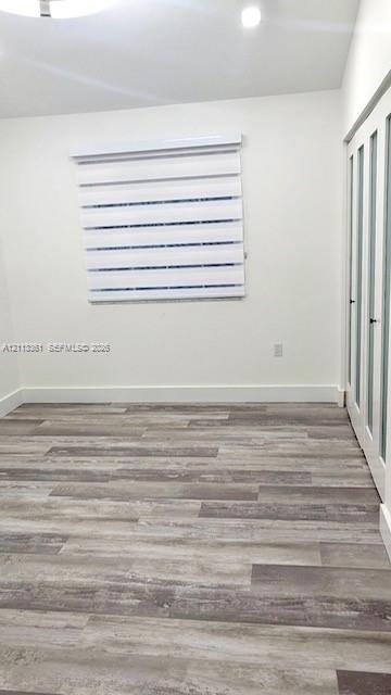 Room featuring wood-finish flooring, recessed lighting, a modern circular ceiling fixture, and dual-layer adjustable roller shades