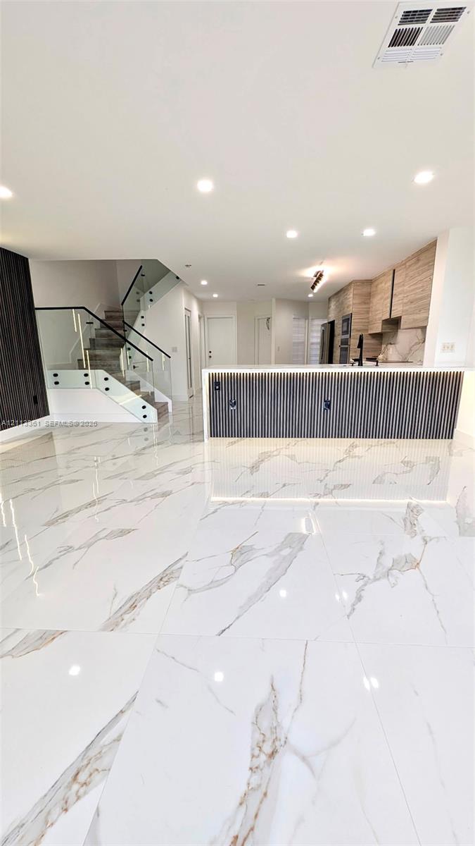Kitchen featuring two-tone cabinetry, stone-finish countertops, full-height backsplash, stainless steel built-in appliances, and large-format tile flooring