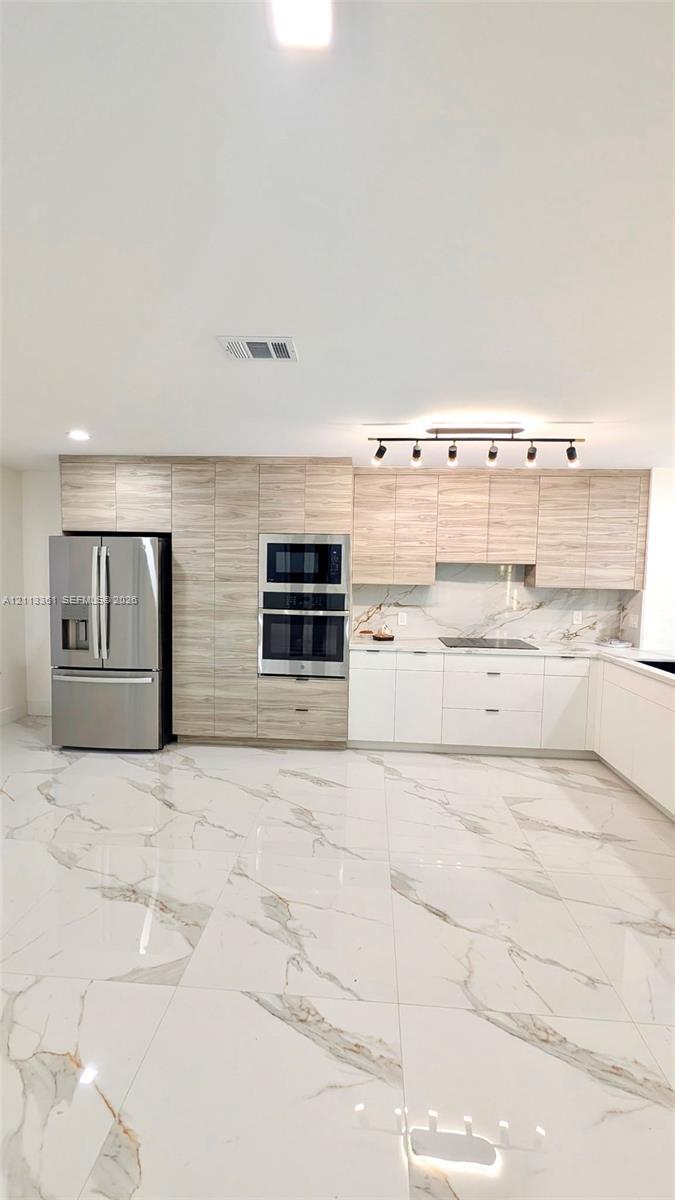 Kitchen featuring white flat-panel cabinetry, light-toned wood-finish upper cabinets, large-format veined tile flooring, a stainless steel dishwasher, and a multi-light track fixture