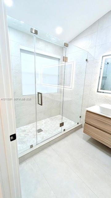 Walk-in shower featuring a frameless glass enclosure, rainfall showerhead with a handheld sprayer, wall-integrated niche, and wood-finish floating vanity with a vessel sink