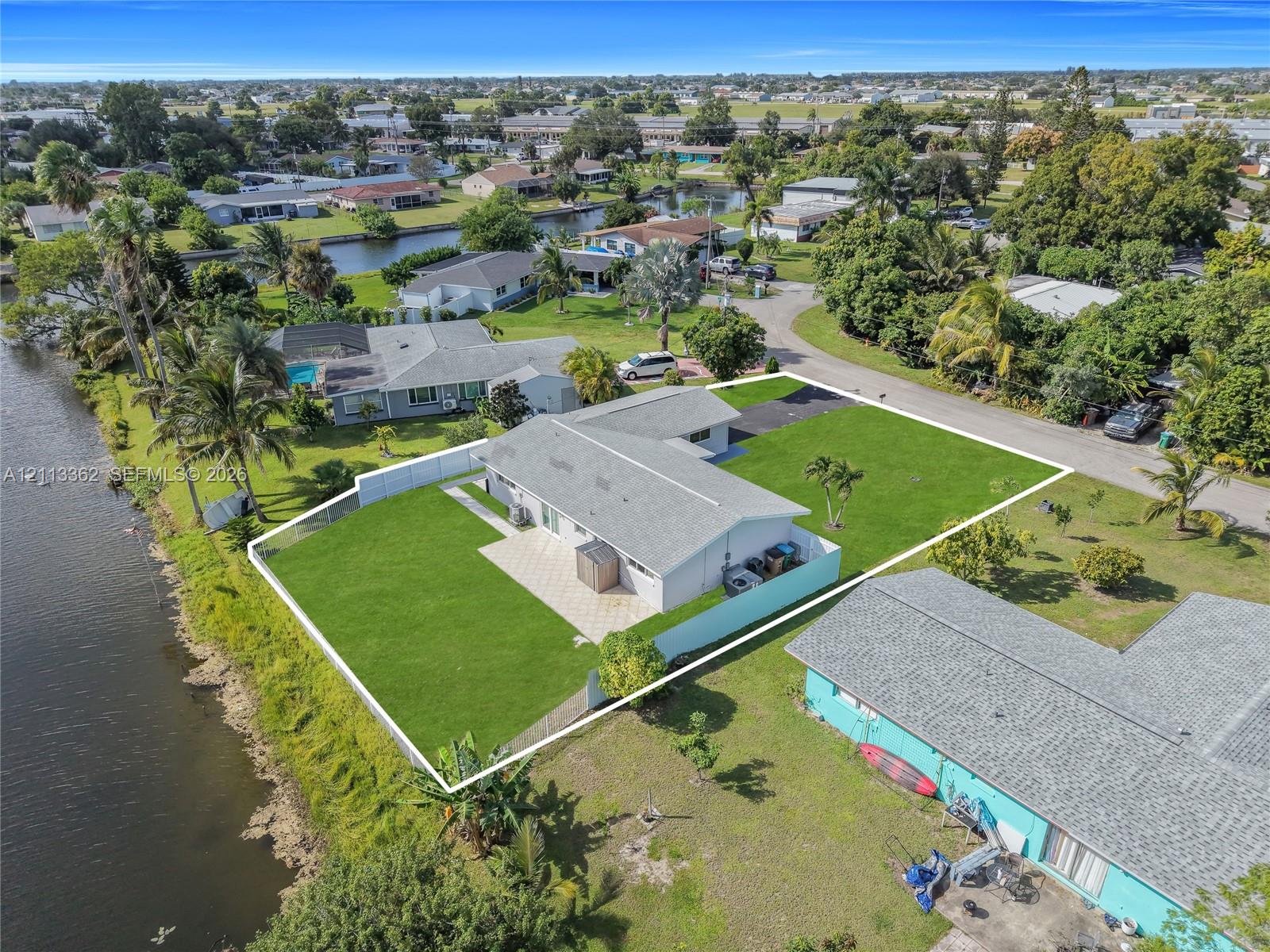 Waterfront property featuring a concrete patio, perimeter fencing, and an expansive lawn