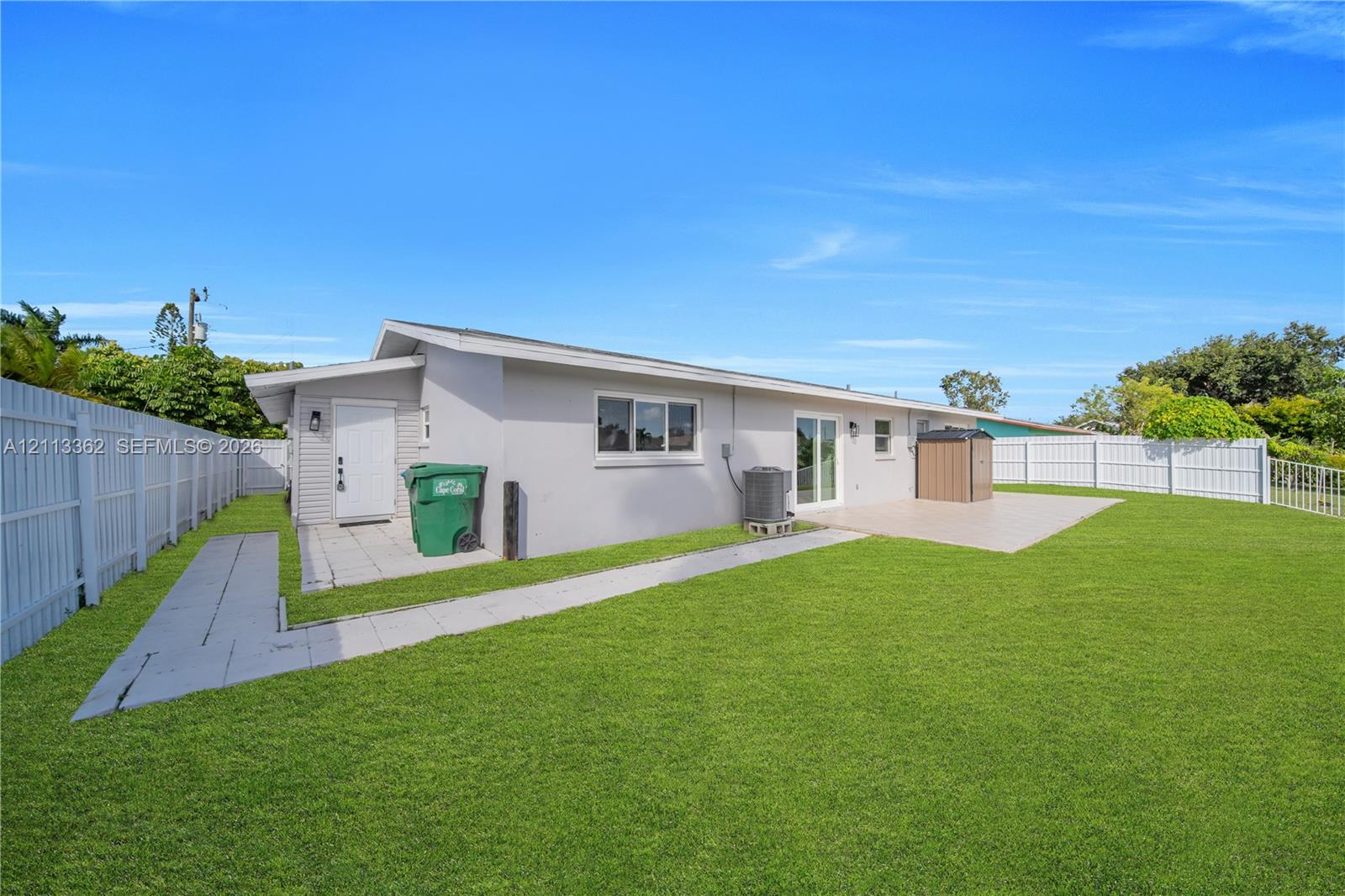 Rear exterior featuring a concrete patio, white vinyl fencing, and a manicured lawn