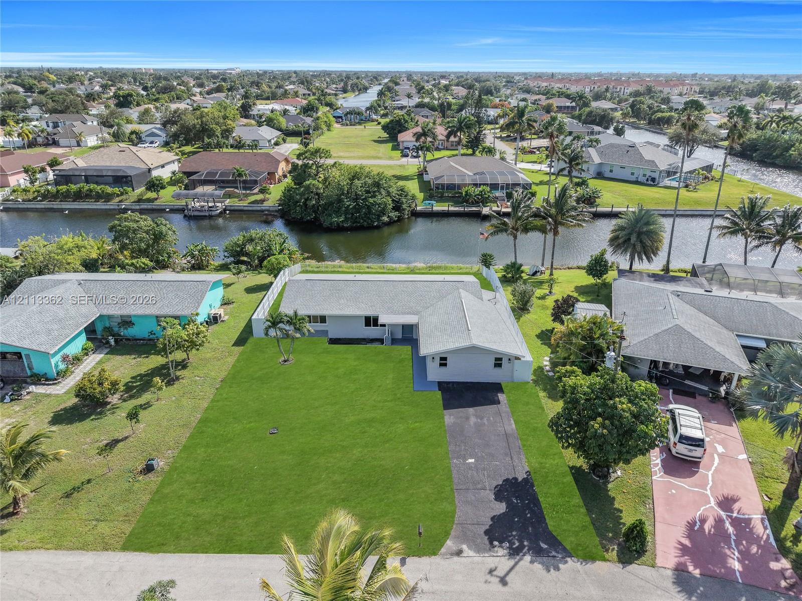 Single-story residence featuring an expansive lawn, concrete driveway, white perimeter fencing, and direct waterfront access