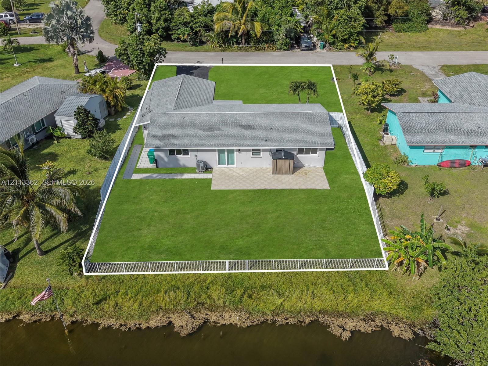 Single-story residence featuring a paved rear patio, expansive fenced yard, and direct waterfront access