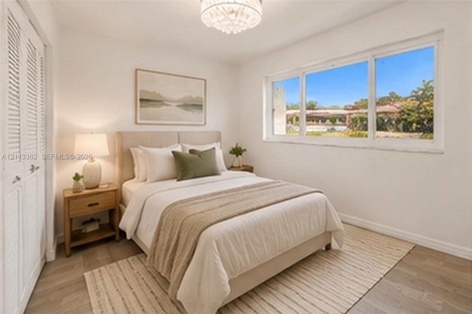 Neutral interior space featuring wood-finish flooring, a crystal-style chandelier, large windows with exterior landscape exposure, and double louvered closet doors