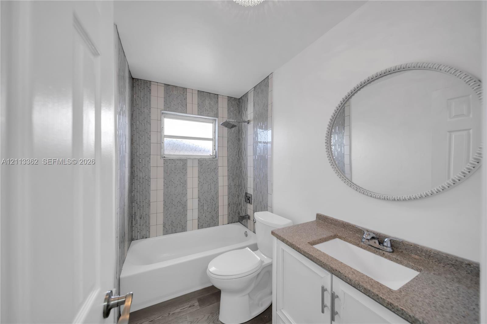 Bathroom featuring a vanity with stone-finish countertop, oval wall-mounted mirror, white tub, and vertical tile shower surround