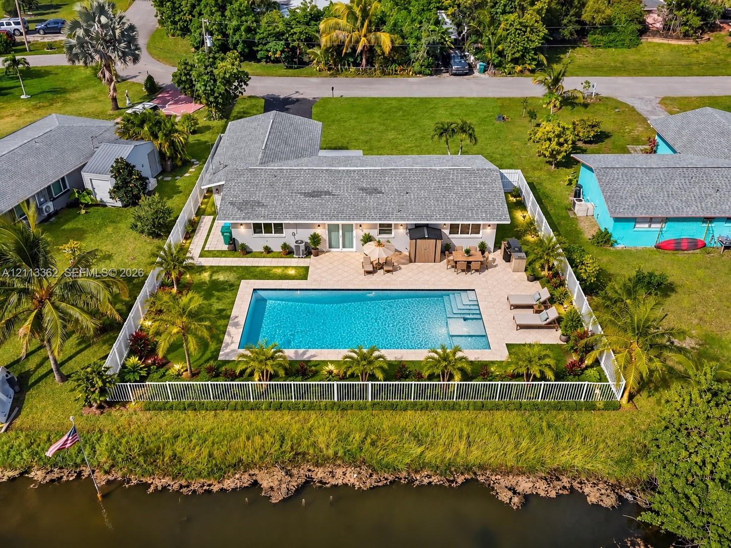 Waterfront exterior featuring a rectangular in-ground swimming pool, expansive paver patio, privacy fencing, and lush landscaping Waterfront exterior featuring a rectangular in-ground swimming pool, expansive paver patio, privacy fencing, and lush landscaping