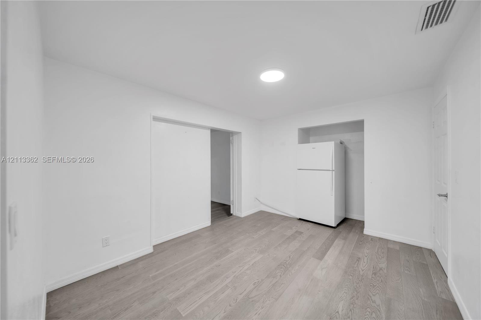 Interior space featuring wood-finish flooring, recessed ceiling lighting, and a white top-mount refrigerator set within a recessed alcove