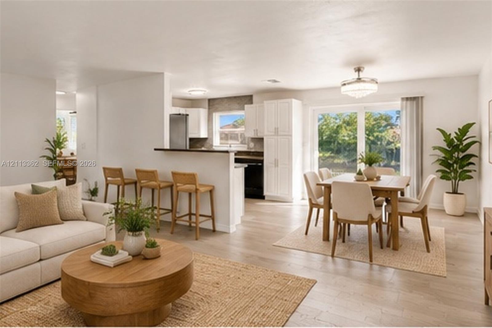 Open-concept living space featuring wood-finish flooring, white cabinetry, a breakfast bar with stone-look countertop, and large glass sliding doors