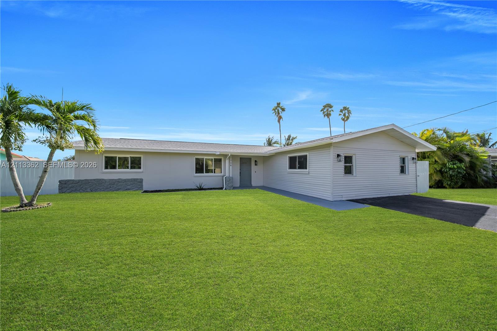 Single-story residence featuring light-toned horizontal siding, a gray shingled roof, asphalt driveway, and expansive lawn area