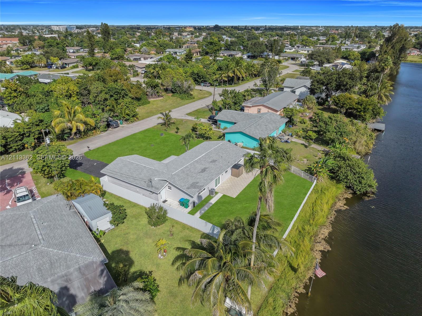 Aerial perspective featuring waterfront property with a concrete patio, expansive lawn, mature palms, and direct canal access