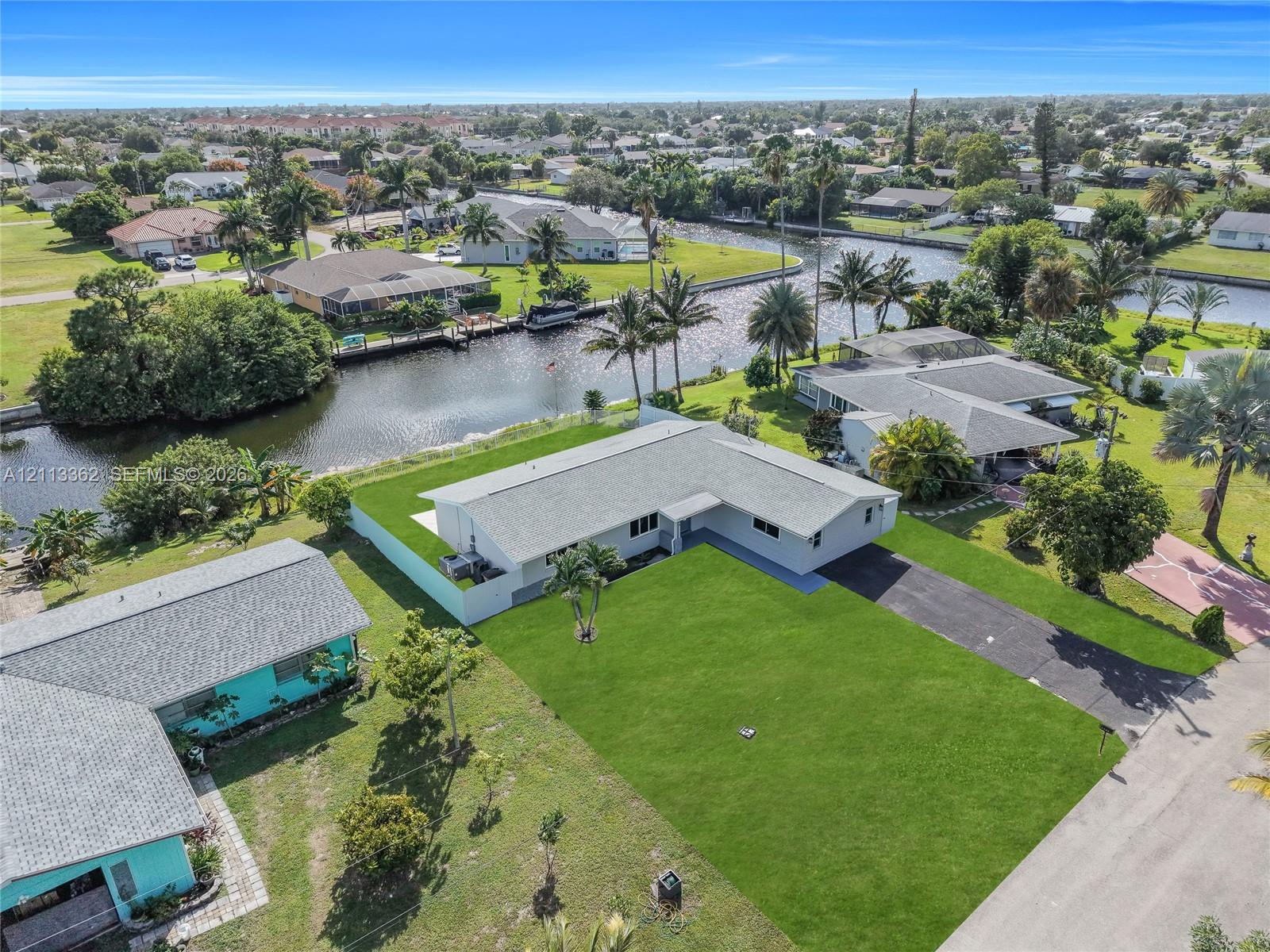 Aerial view of a waterfront property featuring a canal-side lot, expansive lawn, asphalt driveway, and shingle-style roof
