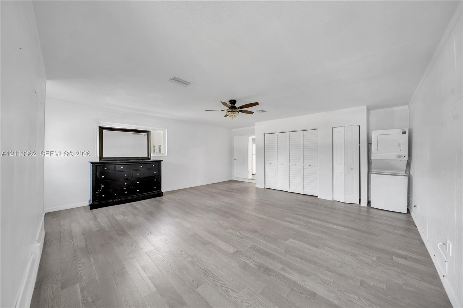 Wood-finish flooring, multi-panel bi-fold closet doors, integrated ceiling fan with light fixture, and stacked laundry unit